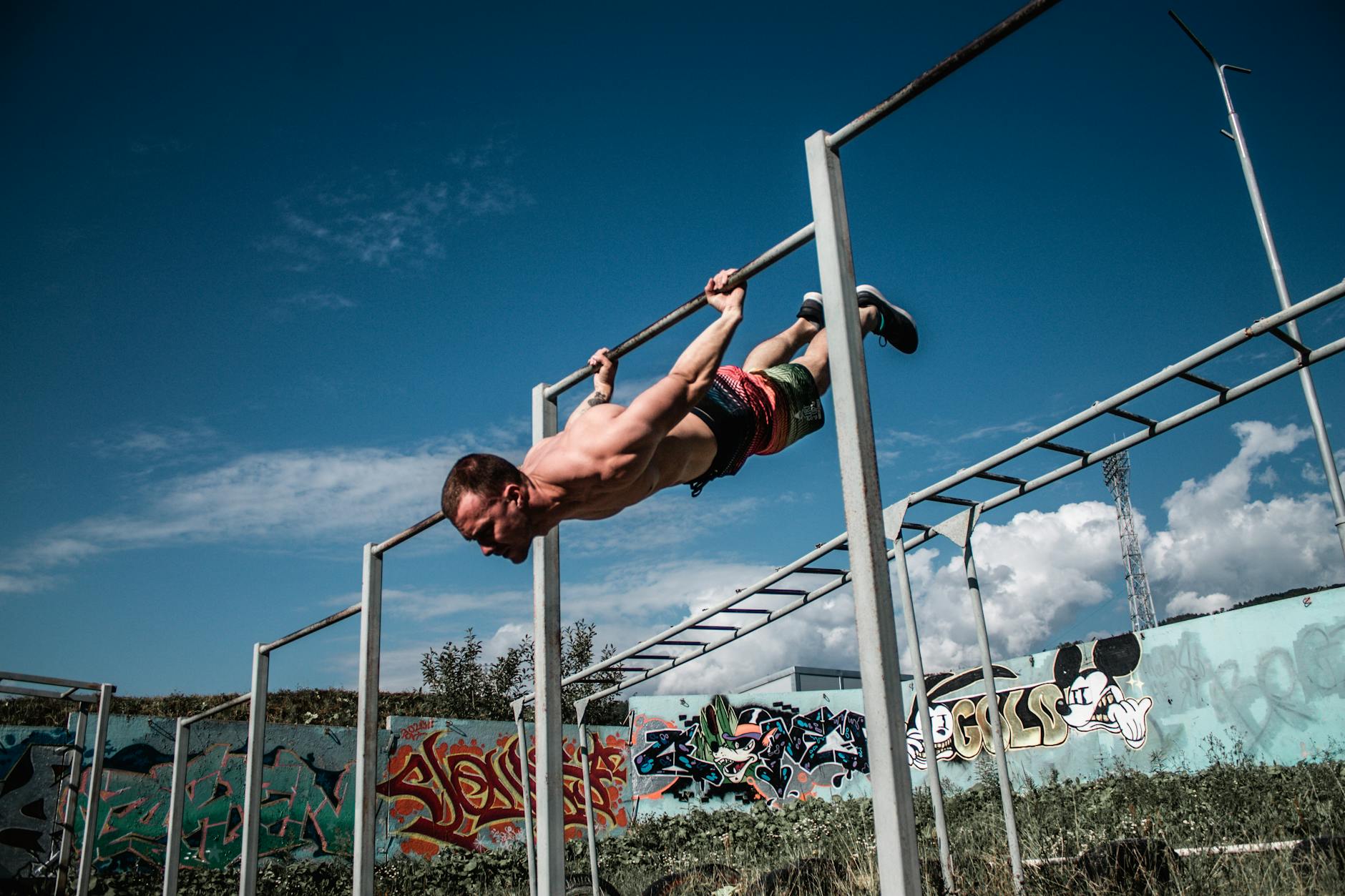 Mężczyzna wykonuje flagę na drążku na zewnętrznej siłowni z graffiti