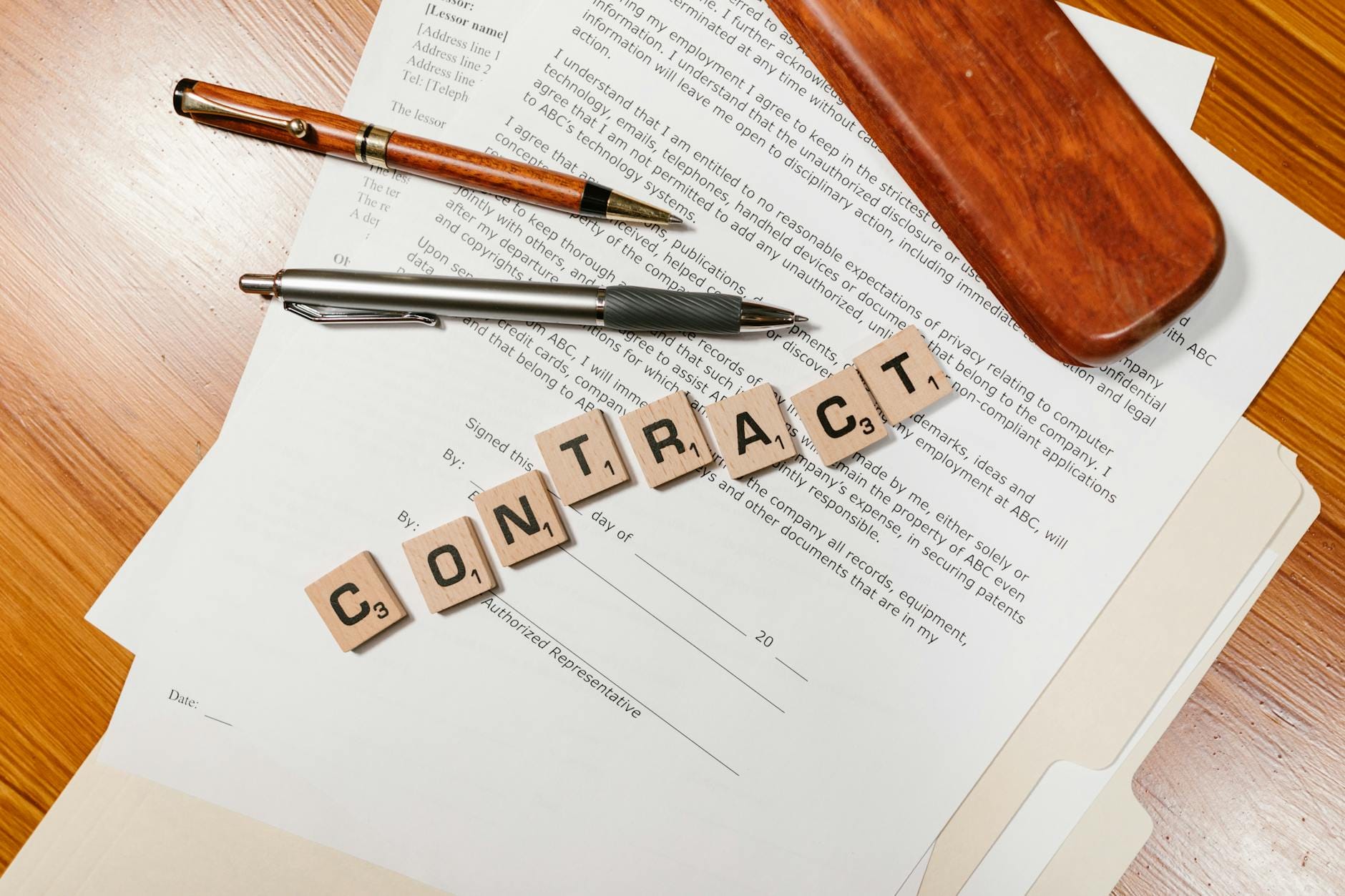 Klocki Scrabble tworzące napis CONTRACT na tle papierów umowy