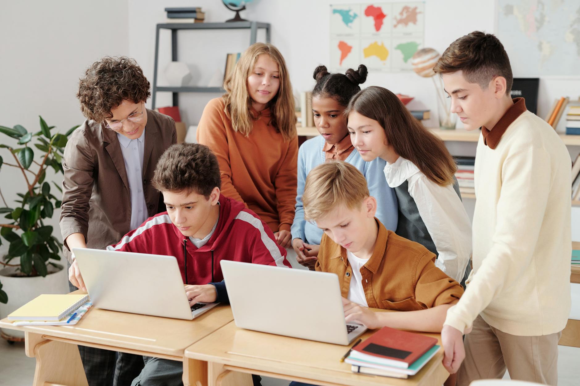 Nauczyciel pomaga zróżnicowanej grupie uczniów pracujących przy laptopach