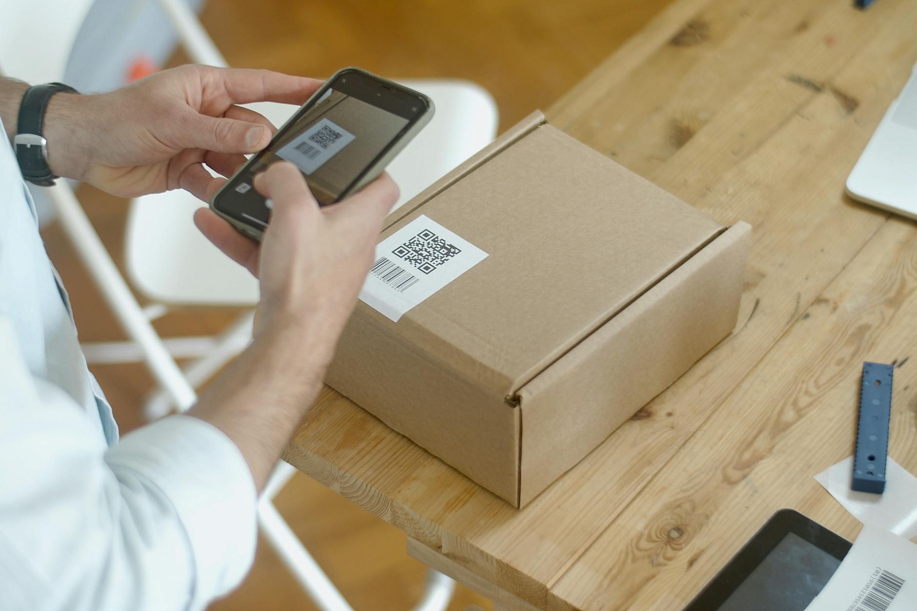 Pracownik skanuje kod QR na paczce smartfonem w magazynie e-commerce