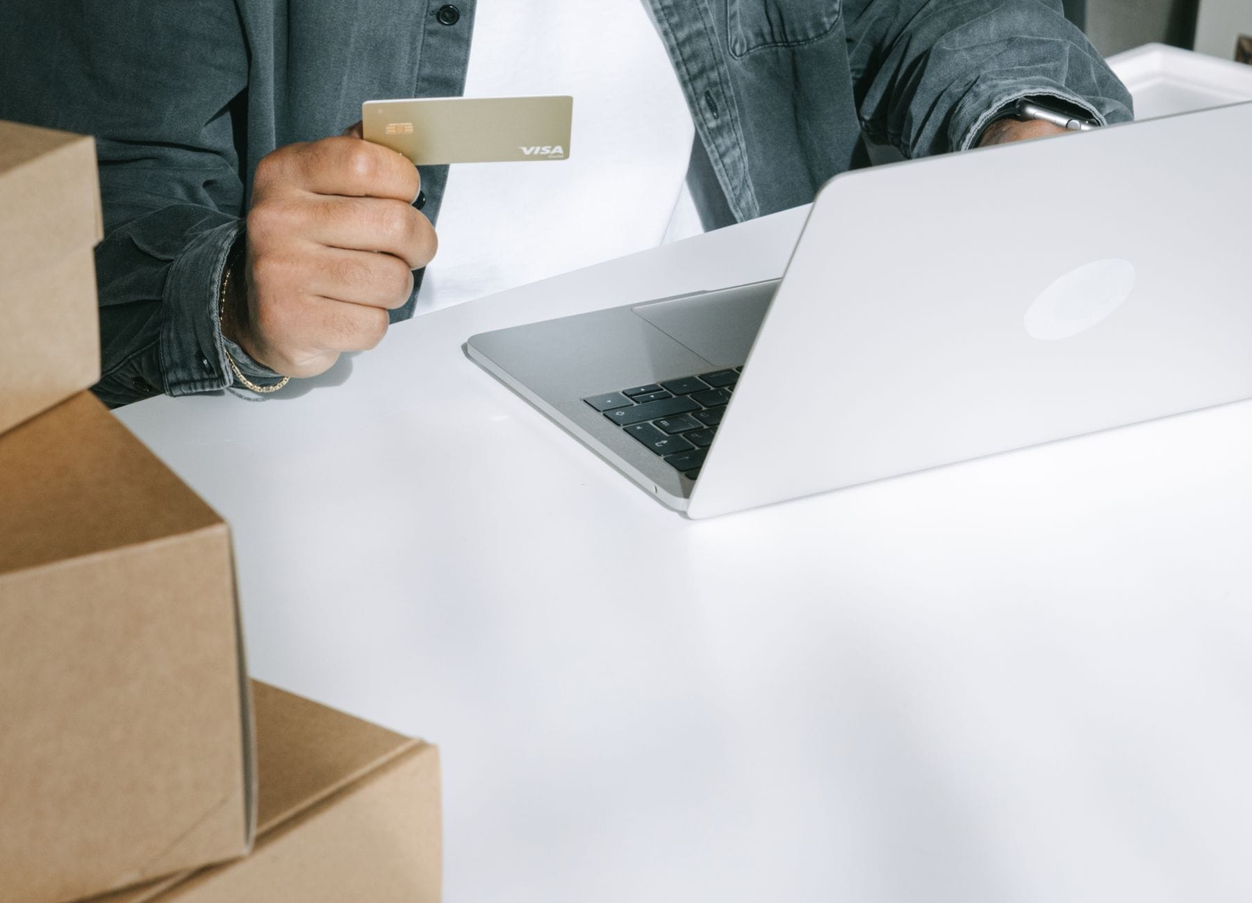 Czym grozi ręczne wystawianie ofert w wielu kanałach i jak to zautomatyzować Osoba płaci kartą za zakupy online na laptopie wśród pudełek wysyłkowych