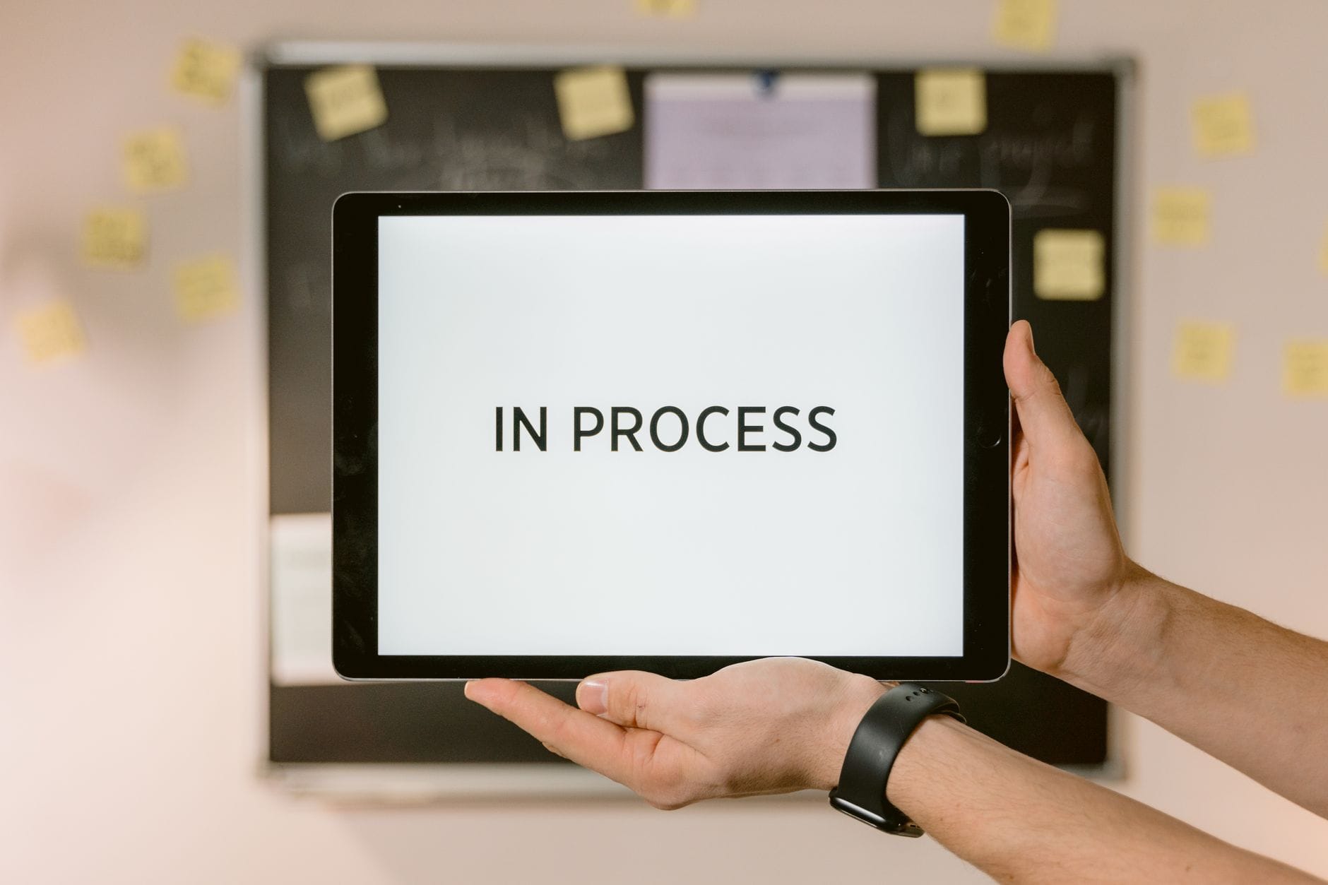Dłonie trzymające tablet z napisem In Process symbolizującym przepływ pracy