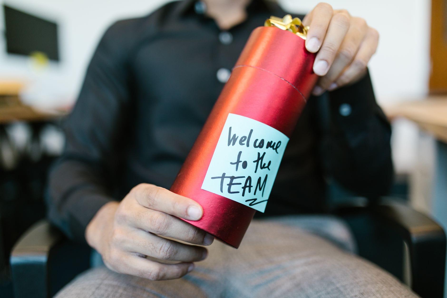 Onboarding klienta krok po kroku: scenariusz w CRM i ERP Osoba trzyma czerwone pudełko prezentowe z kartką welcome to the team